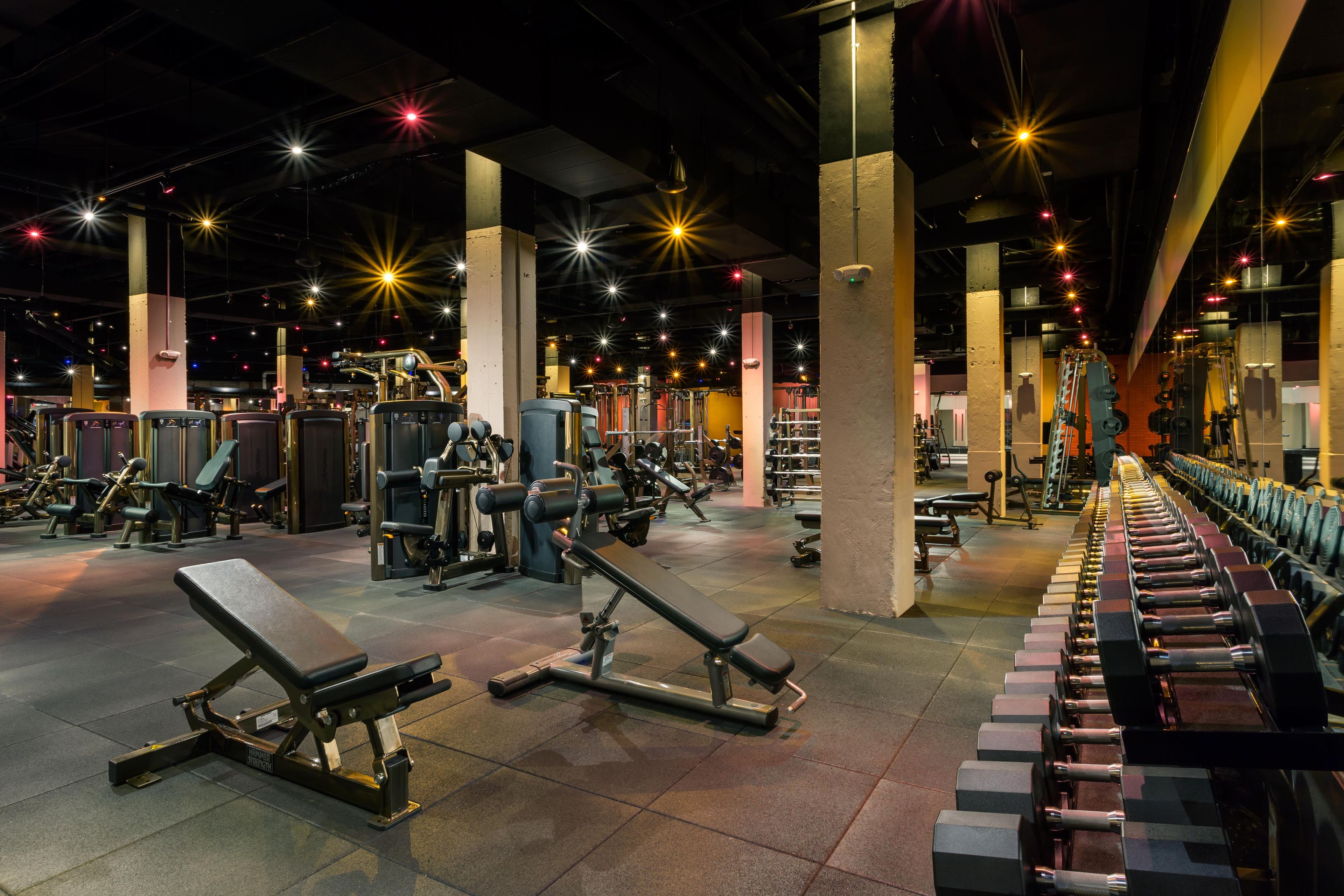 A gym with various exercise equipment, including benches and weight machines, under bright overhead lighting.