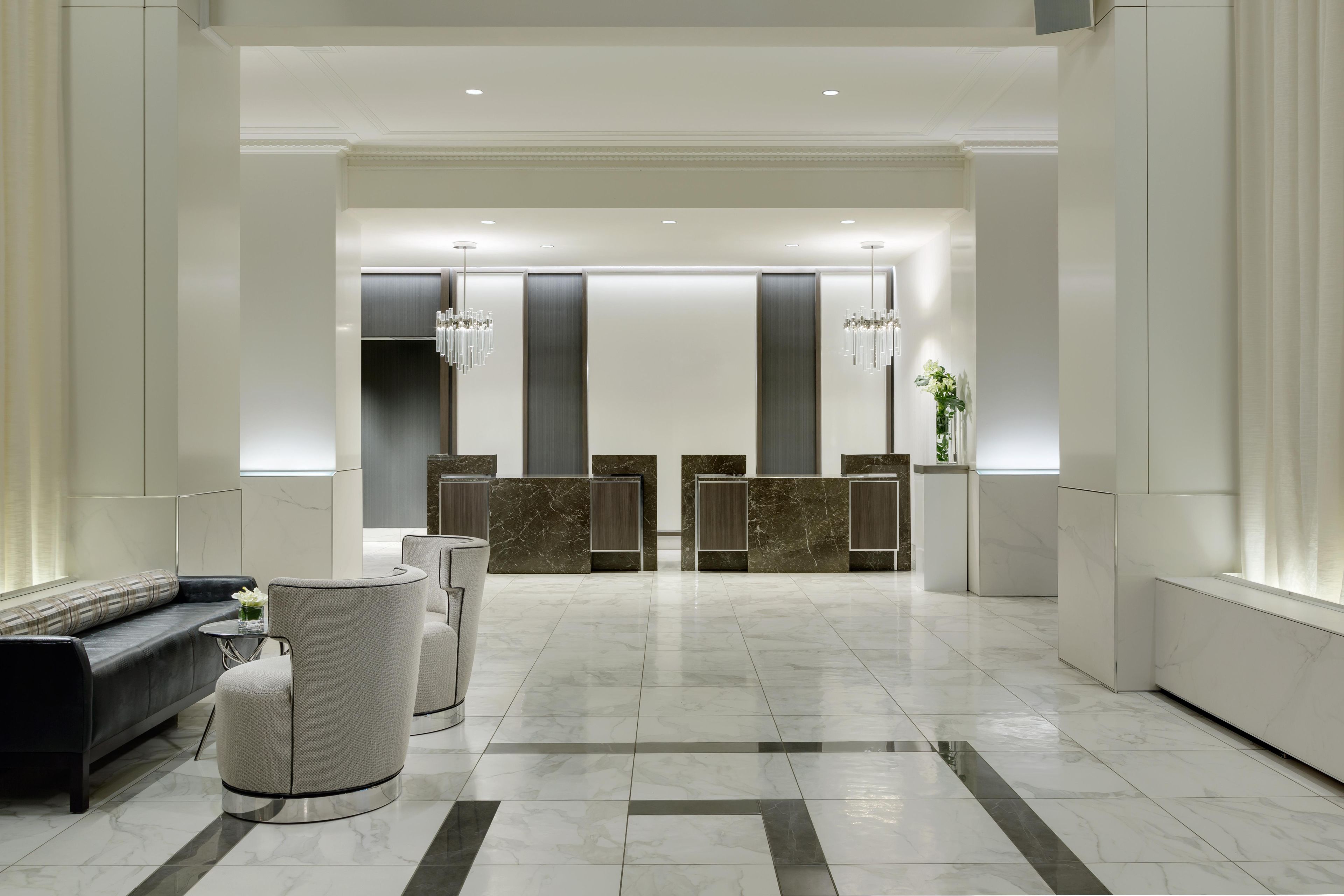 A modern hotel lobby with a reception desk, seating area, and a chandelier.