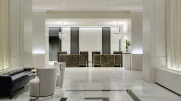 A modern hotel lobby with a reception desk, seating area, and a chandelier.