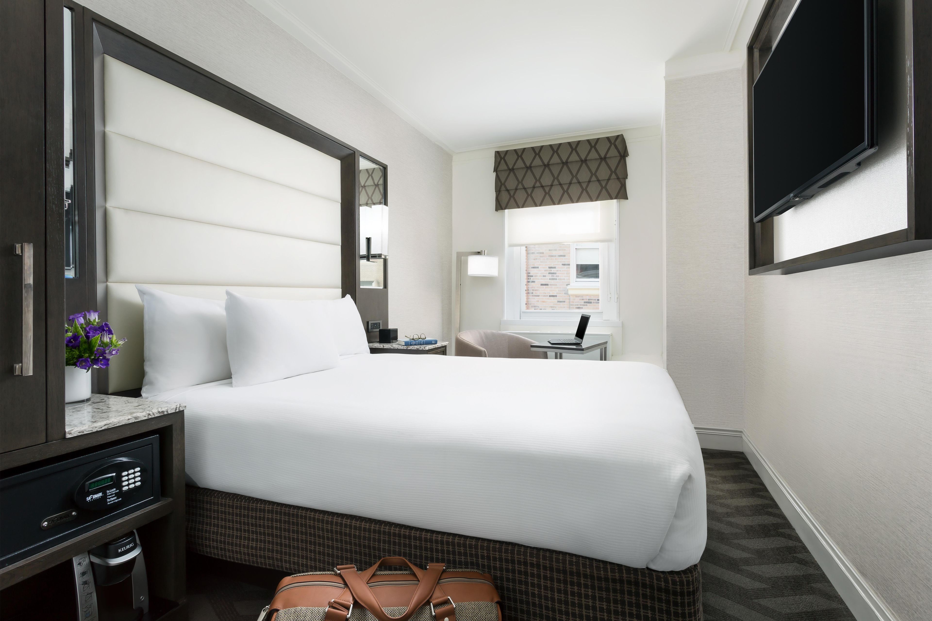 Une chambre d’hôtel avec un lit, un bureau, une chaise, une télévision et une fenêtre.