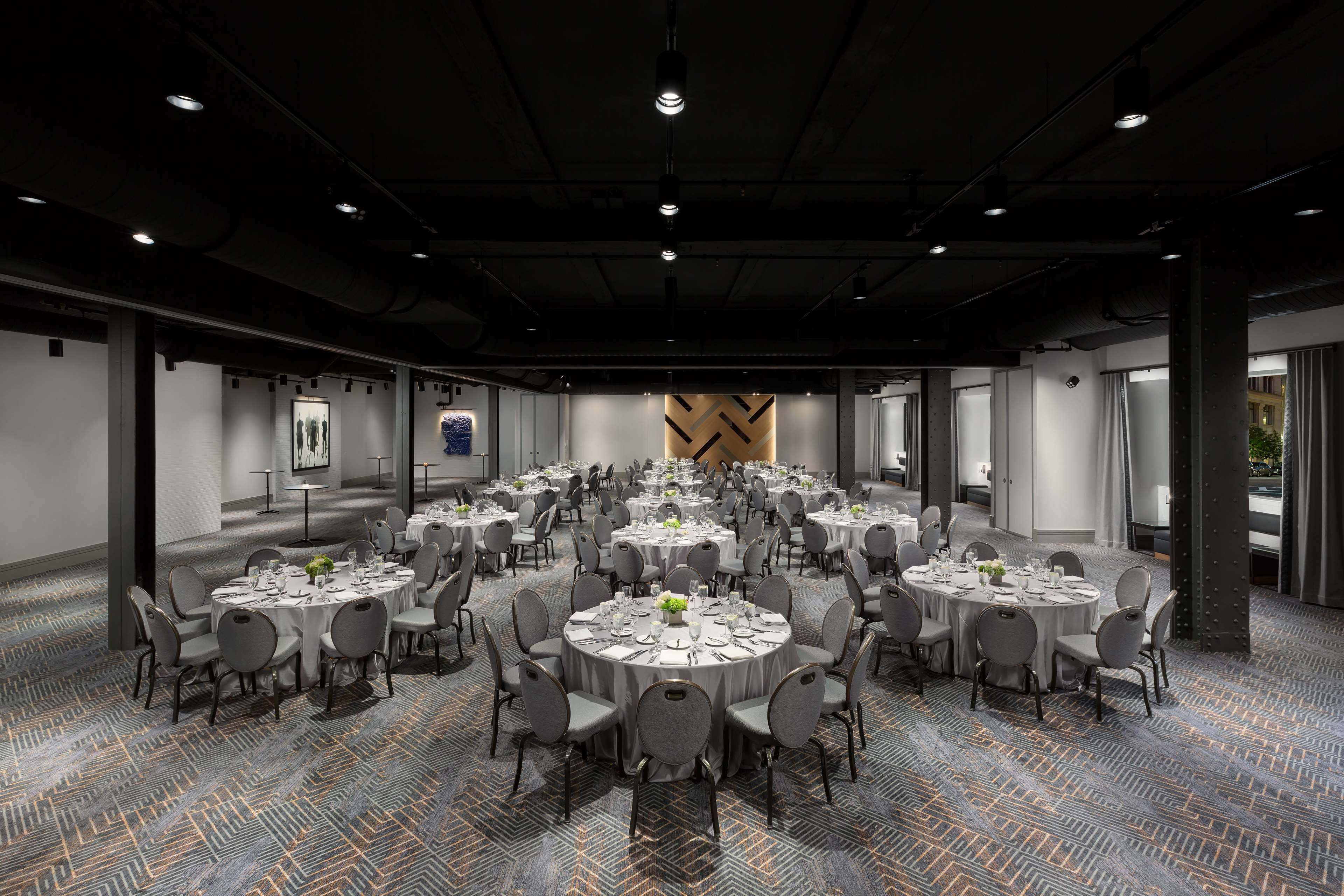 A large conference room with multiple round tables set for dining, equipped with chairs and table settings.