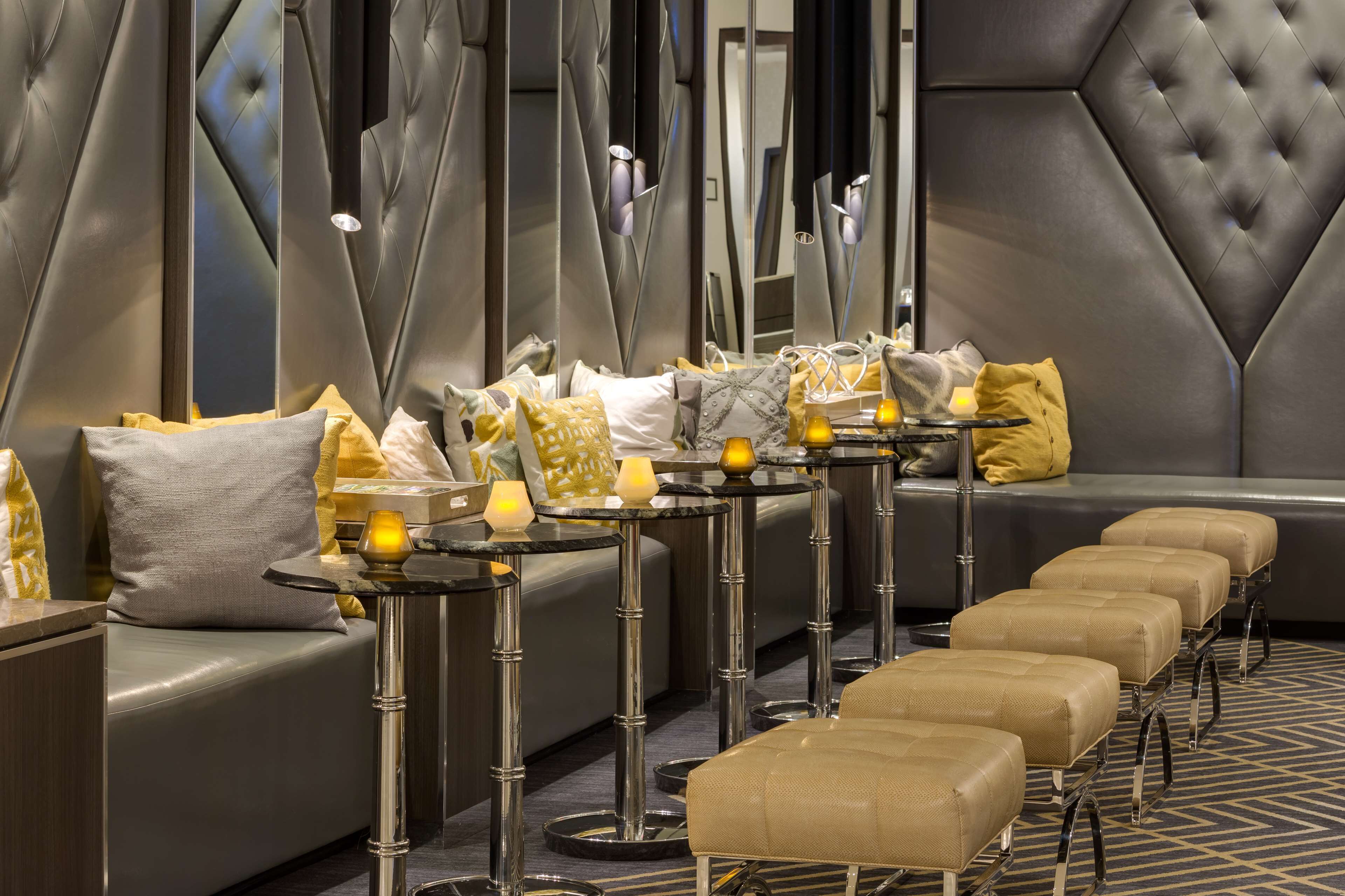 A modern lounge area with leather sofas, a long bench, and a row of small tables with candles.