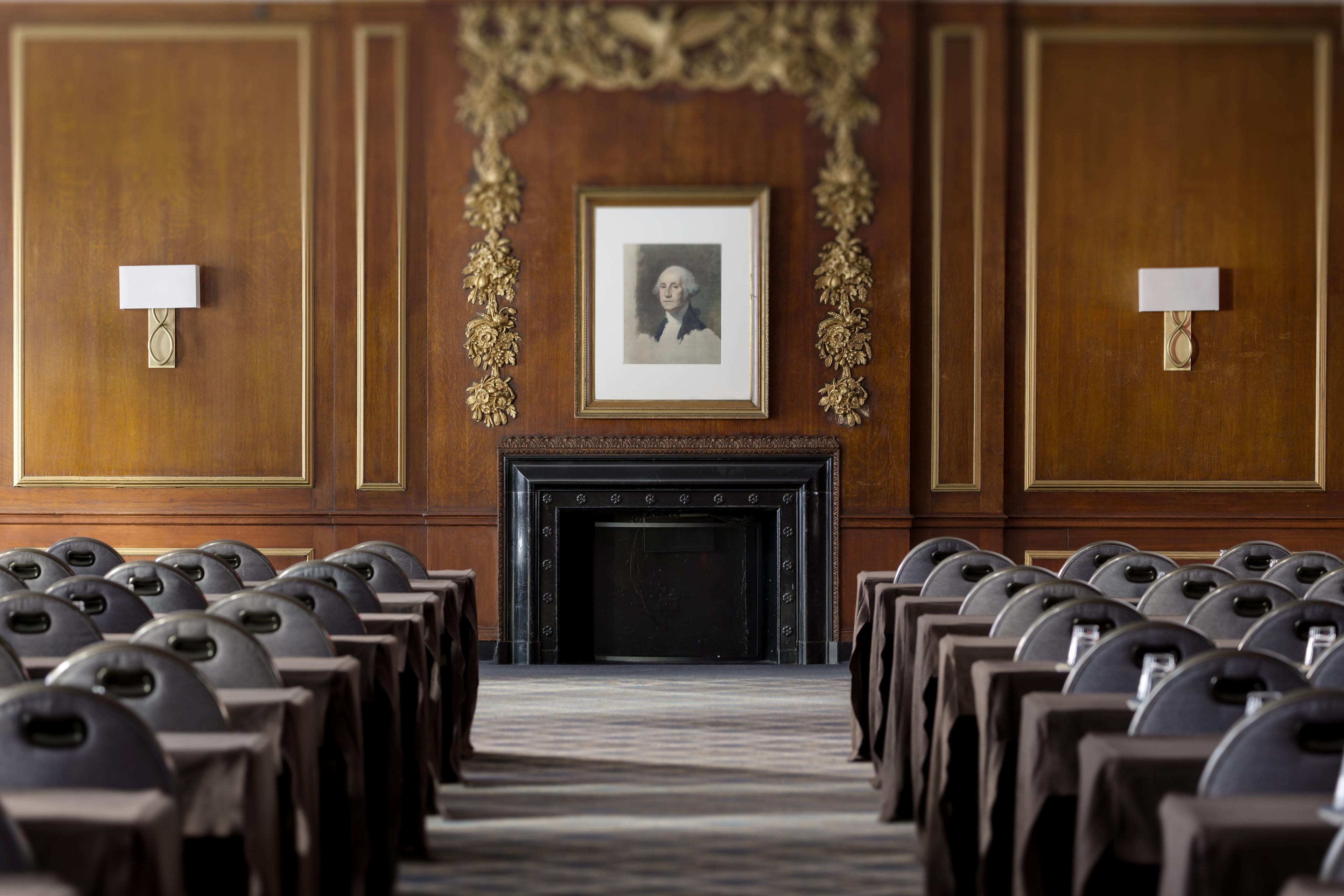 A conference room with rows of chairs, a fireplace, and framed artwork on the wall.