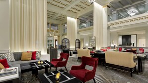 Eine großzügige Lobby mit modernem Design, inklusive einer Couch, Sesseln, einer Essecke und einer breiten Treppe.