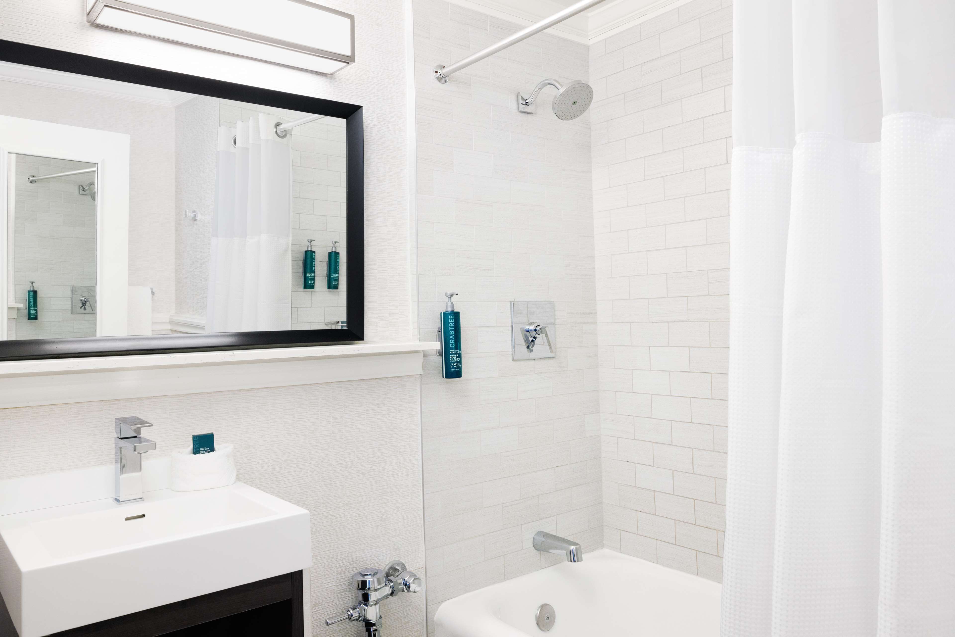 Un baño moderno con un lavamanos blanco, un espejo grande, una ducha con cabezal de ducha manual y un inodoro.