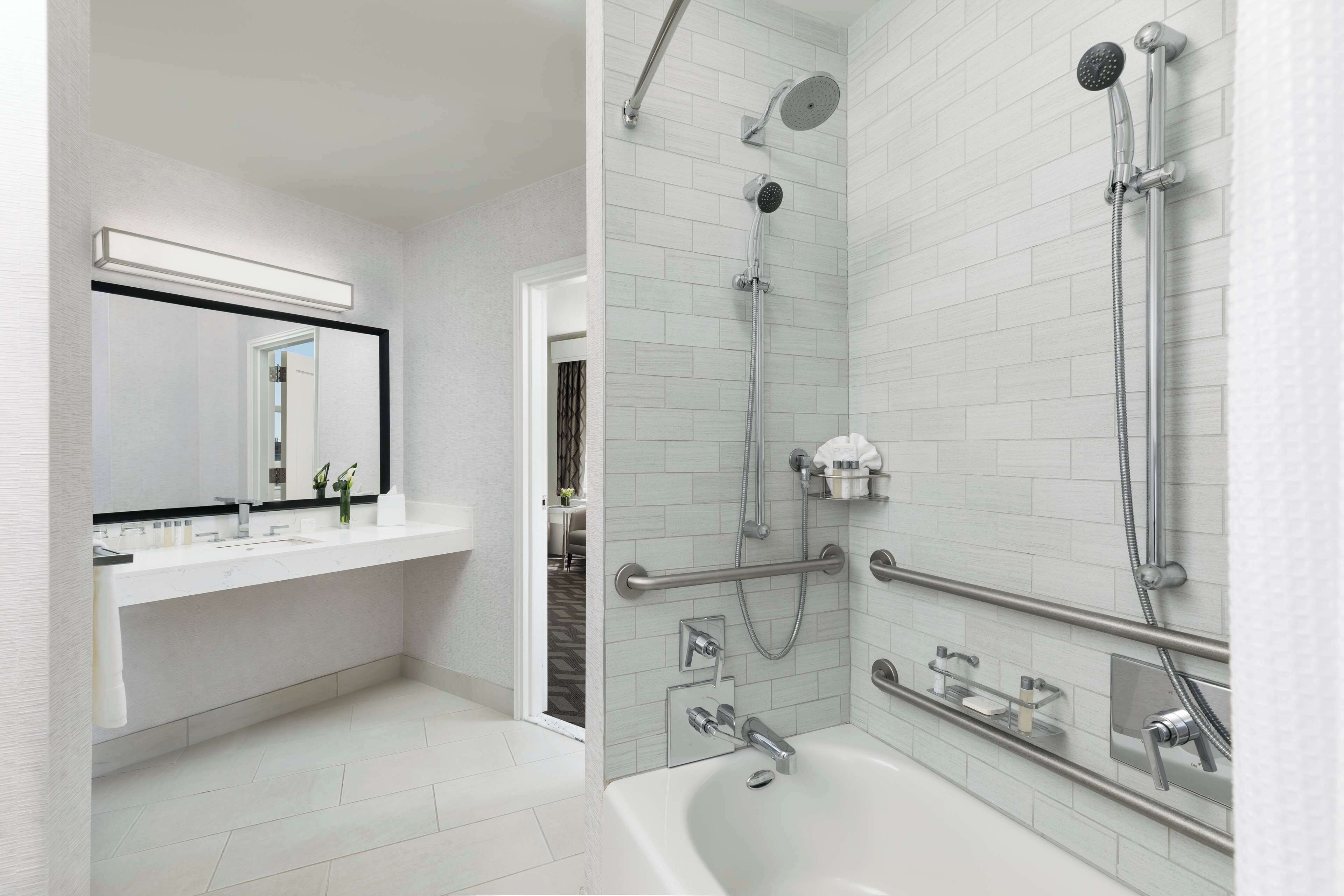 A modern bathroom with a white sink, mirror, and a walk-in shower with a handheld showerhead.