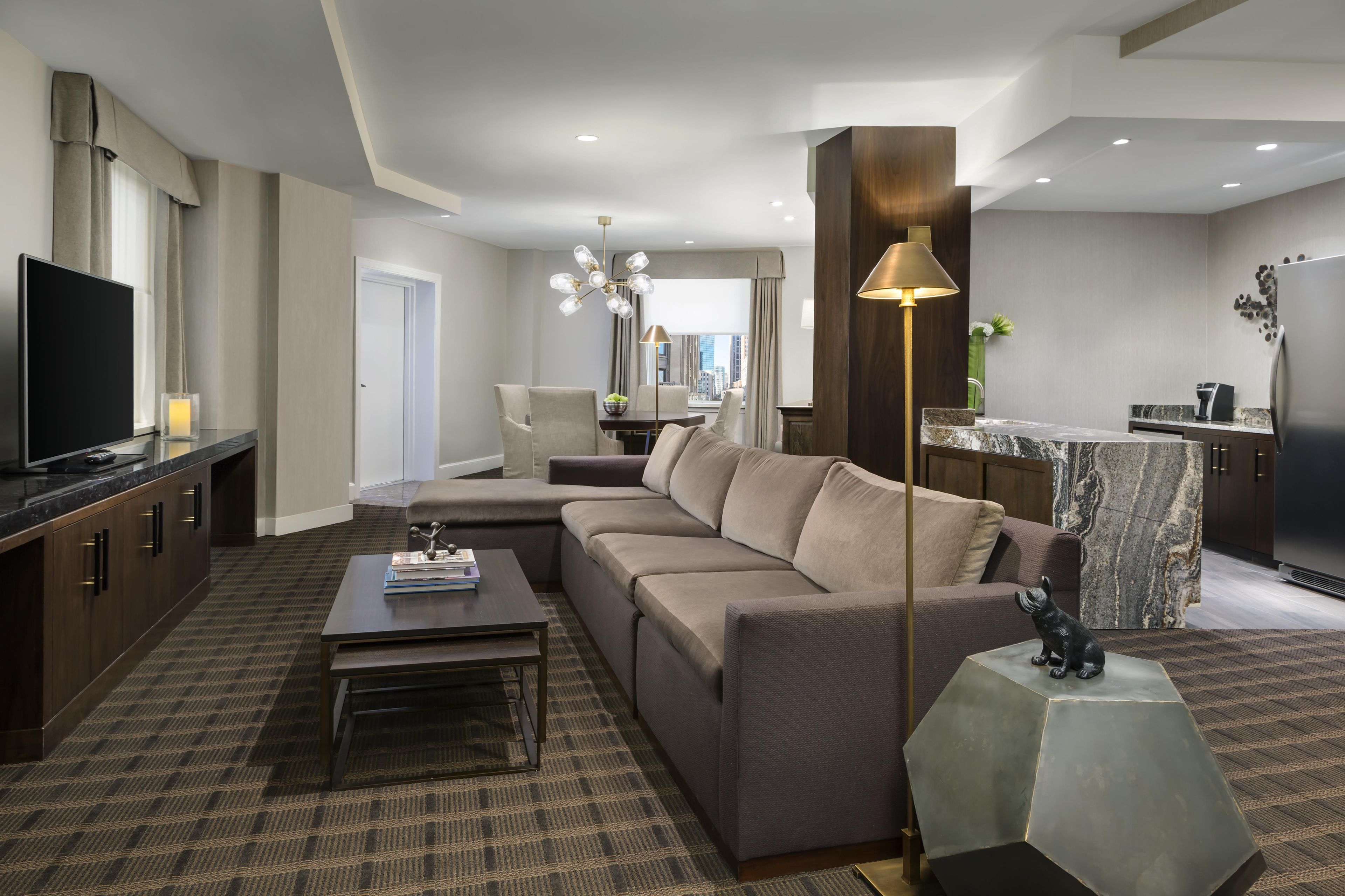 A modern living room with a sectional sofa, a coffee table, a TV, and a dining area with a chandelier.