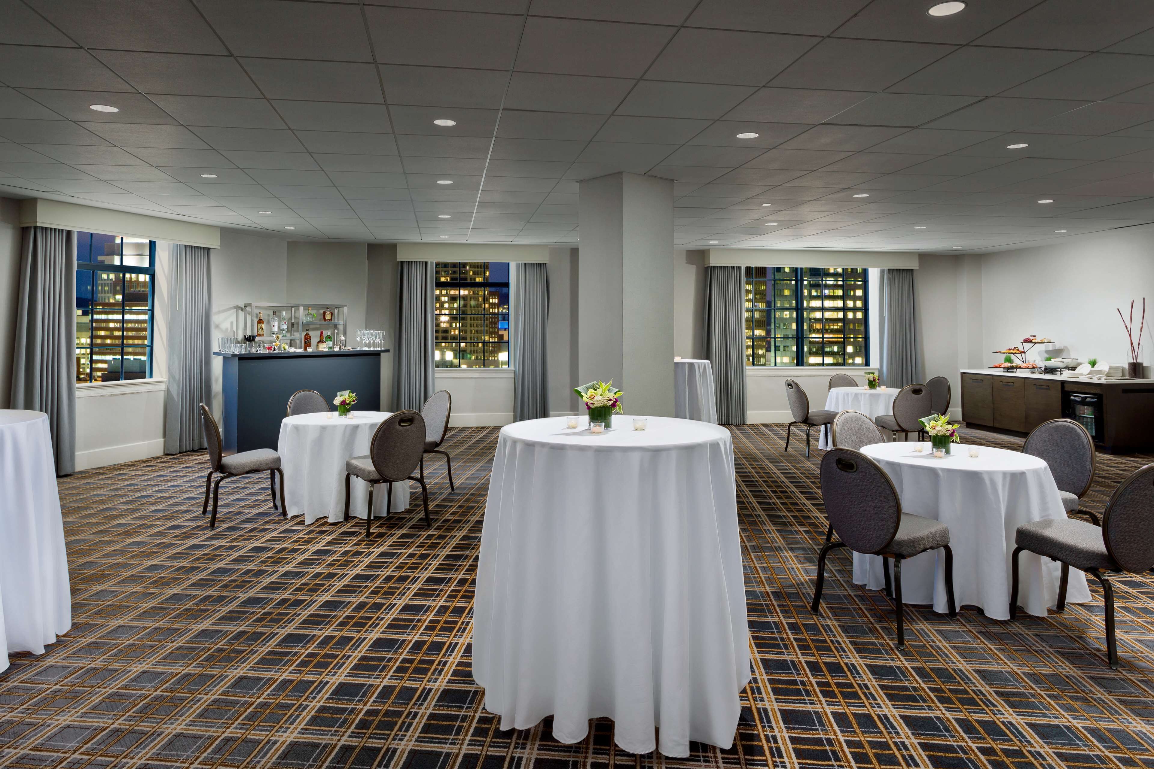 A hotel room with multiple round tables, chairs, and a bar area.