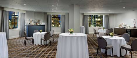 A hotel room with multiple round tables, chairs, and a bar area.