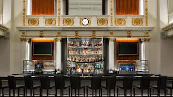 A bar area with a long counter, multiple shelves of bottles, and a clock above.