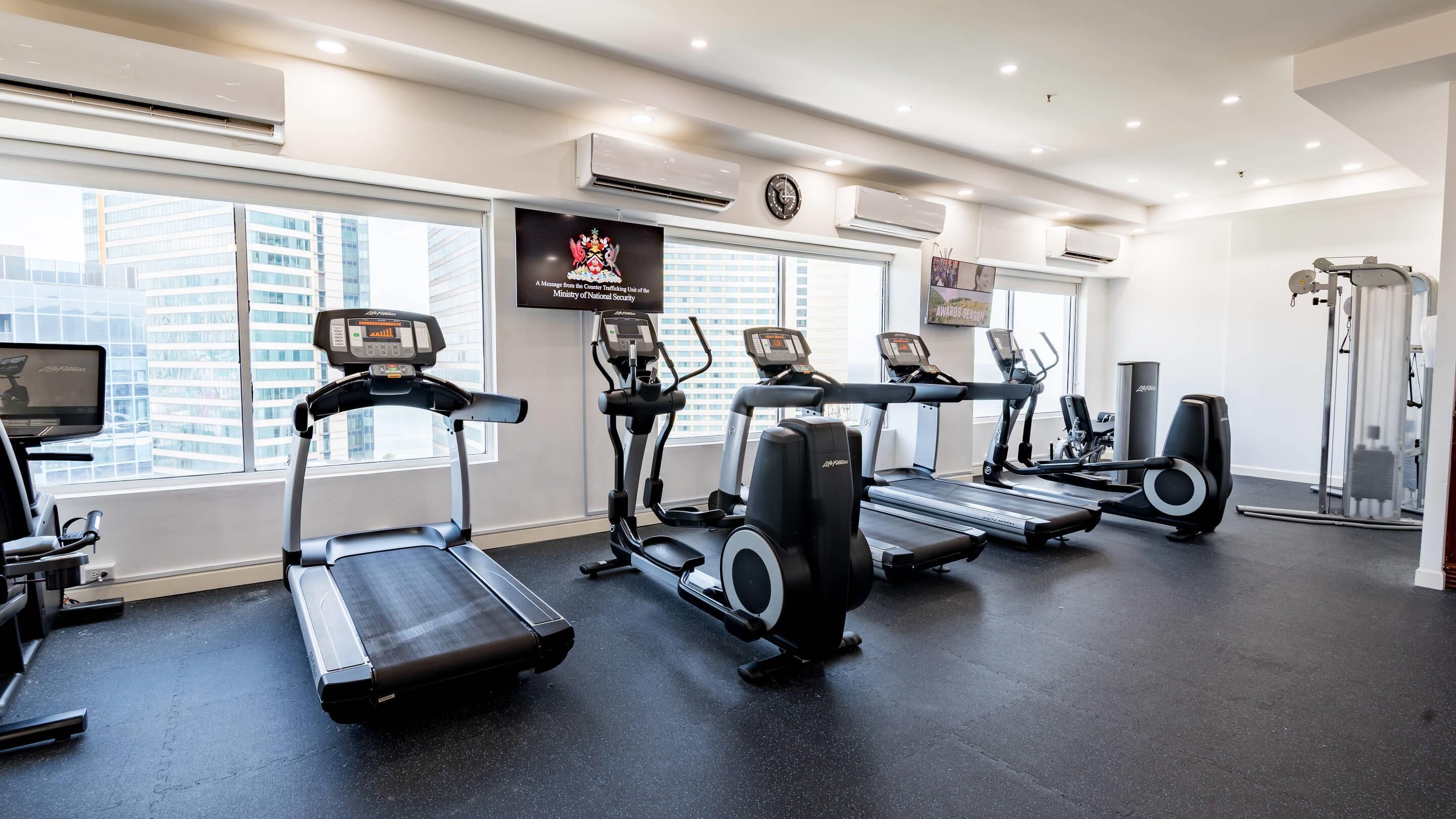 A gym with treadmills, ellipticals, and a TV screen.
