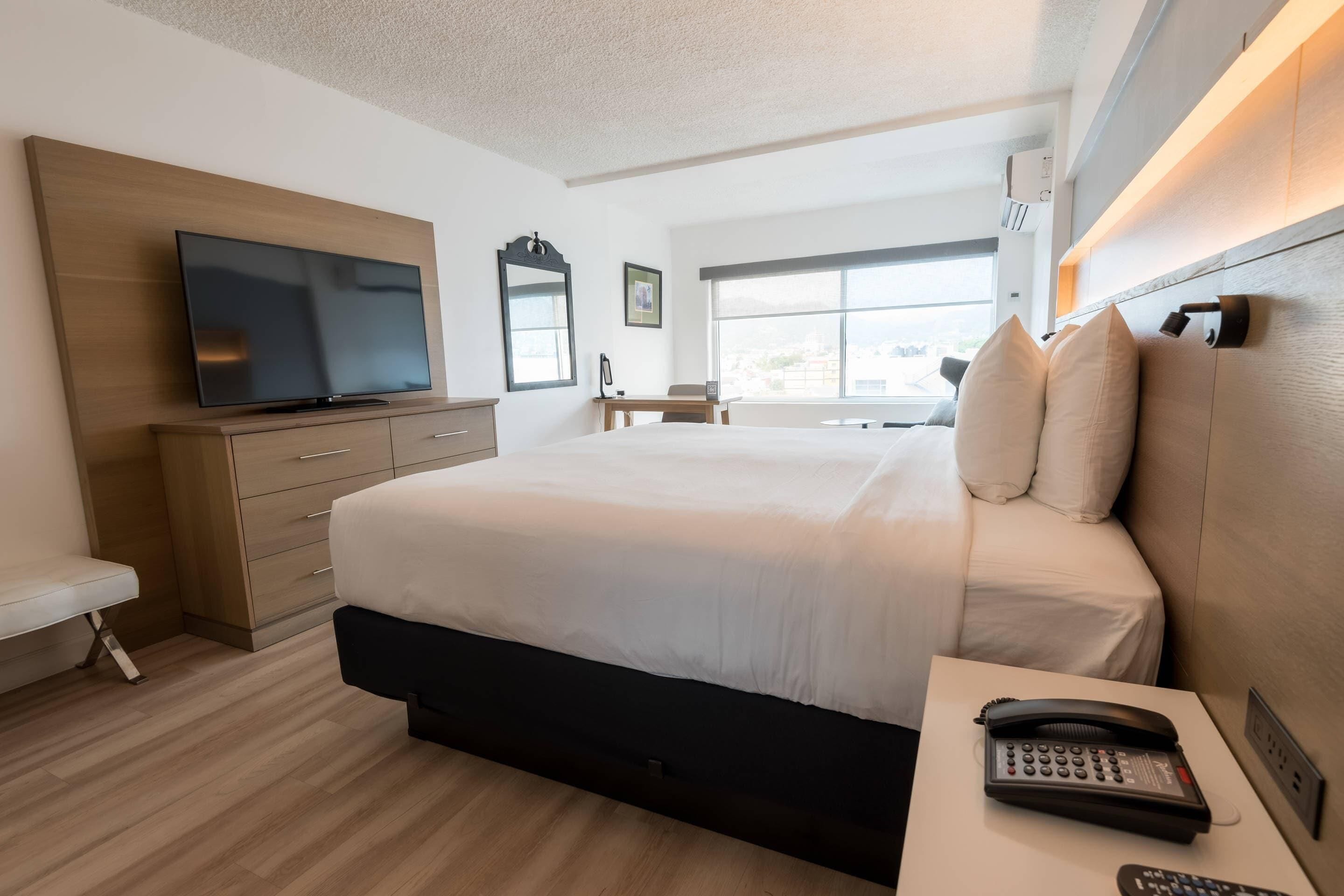 Una habitación de hotel moderna con una cama grande, un televisor de pantalla plana, un escritorio y una ventana con vista a la ciudad.