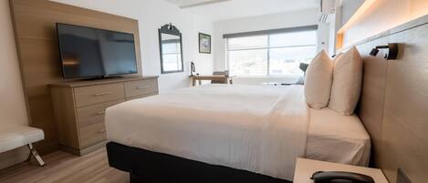 Una habitación de hotel moderna con una cama grande, un televisor de pantalla plana, un escritorio y una ventana con vista a la ciudad.