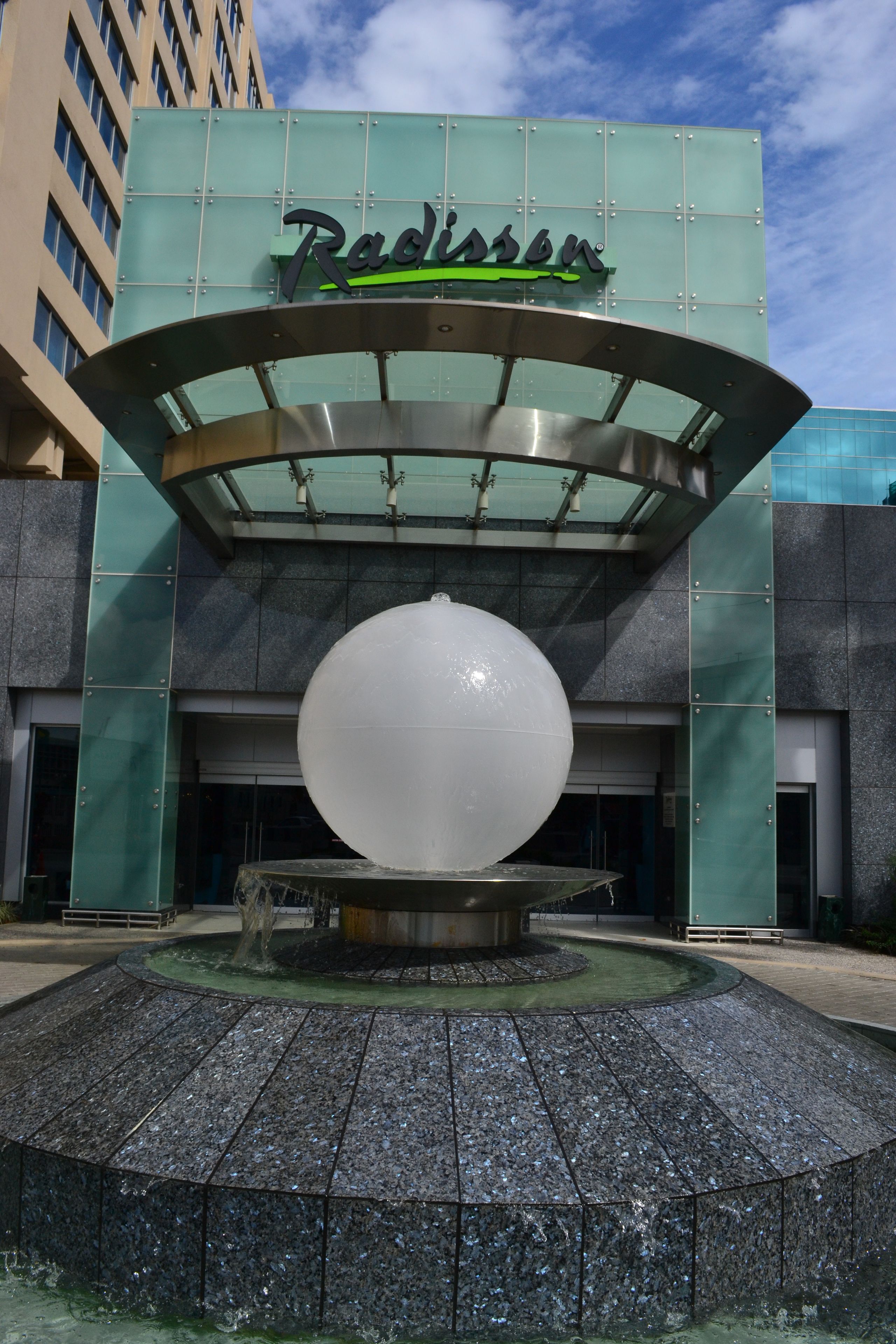 Entrada de um hotel Radisson com uma grande fonte esférica na frente.
