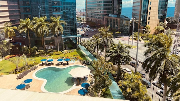 A hotel with a swimming pool, palm trees, and a view of the ocean.