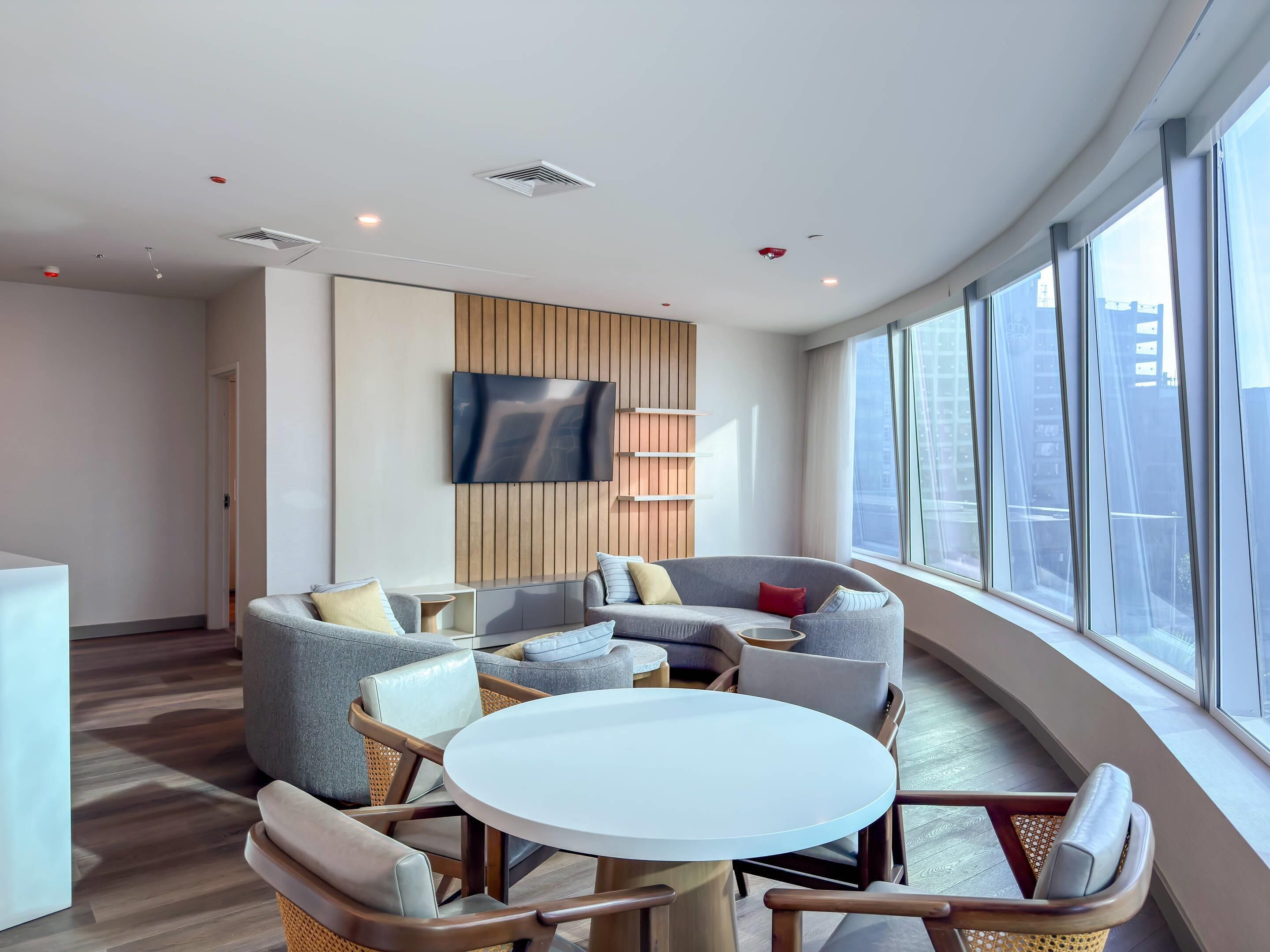 Una sala de estar moderna con techo curvo, pared de paneles de madera integrada, televisor de pantalla plana y un amplio ventanal con vistas a la ciudad.