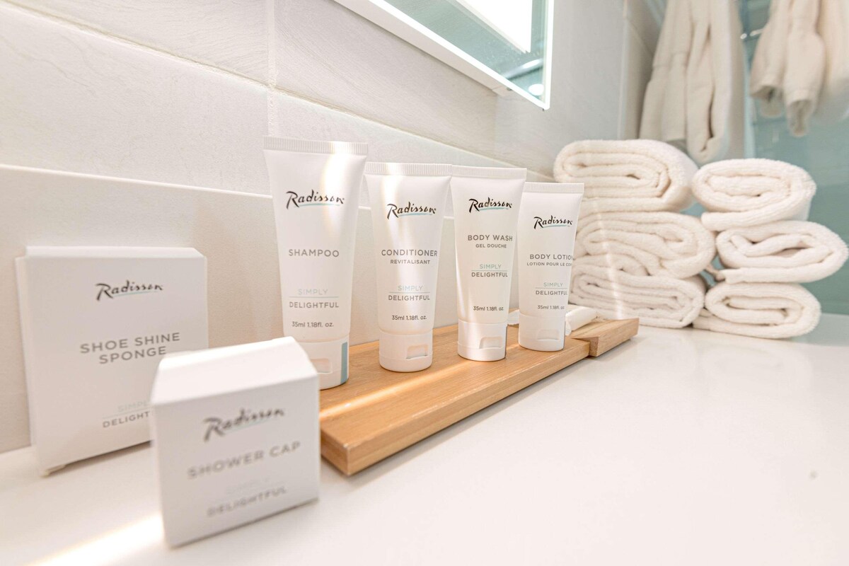 A bathroom with Radisson toiletries including shampoo, conditioner, body wash, and shower cap.