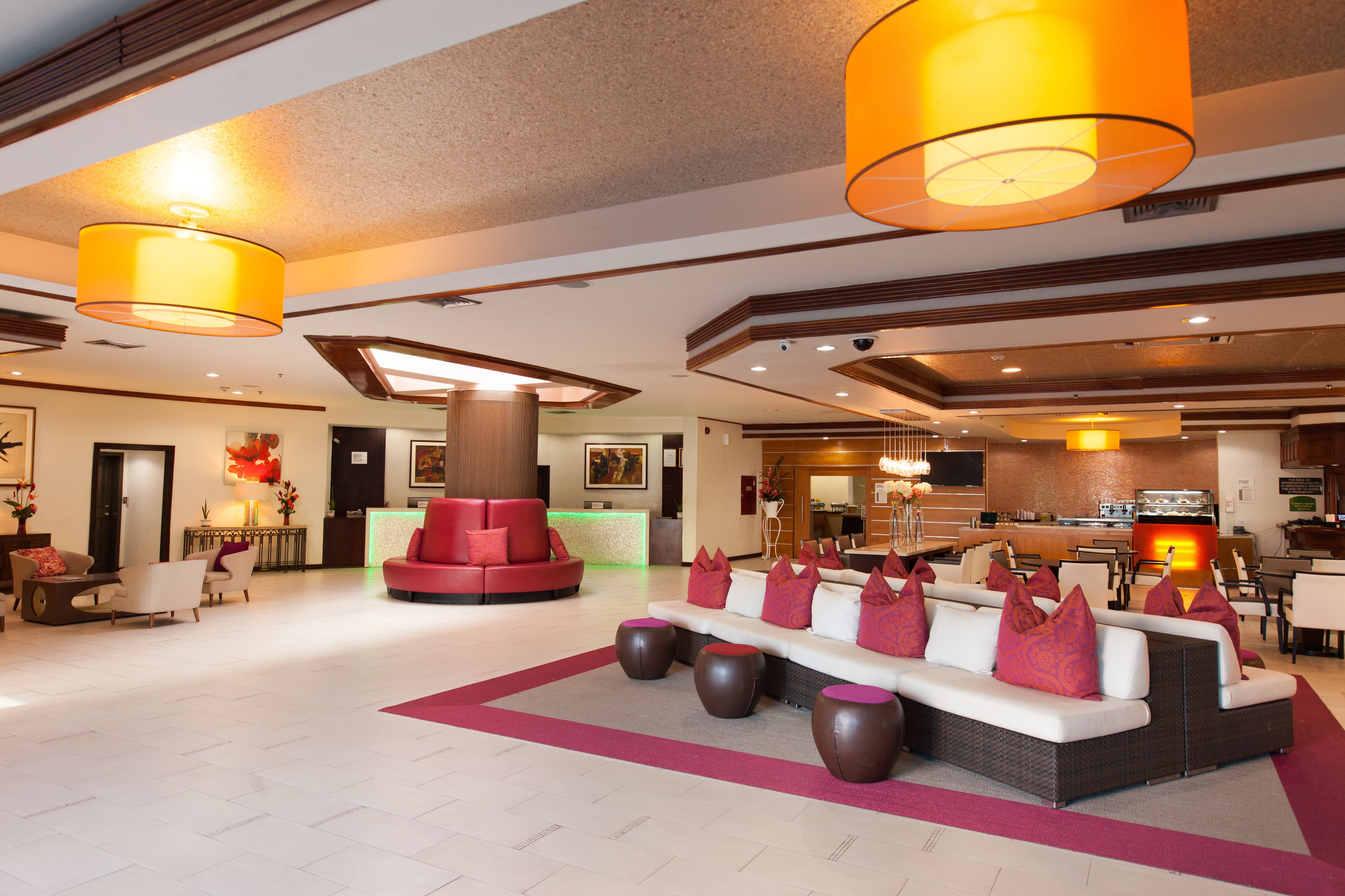 A spacious lobby with a central seating area, a reception desk, and a kitchen in the background.