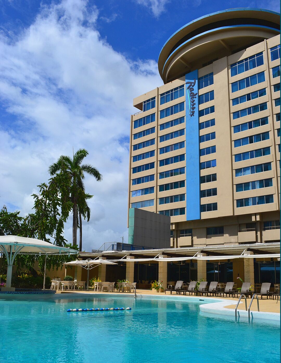 A hotel with a large pool, palm trees, and a clear blue sky.