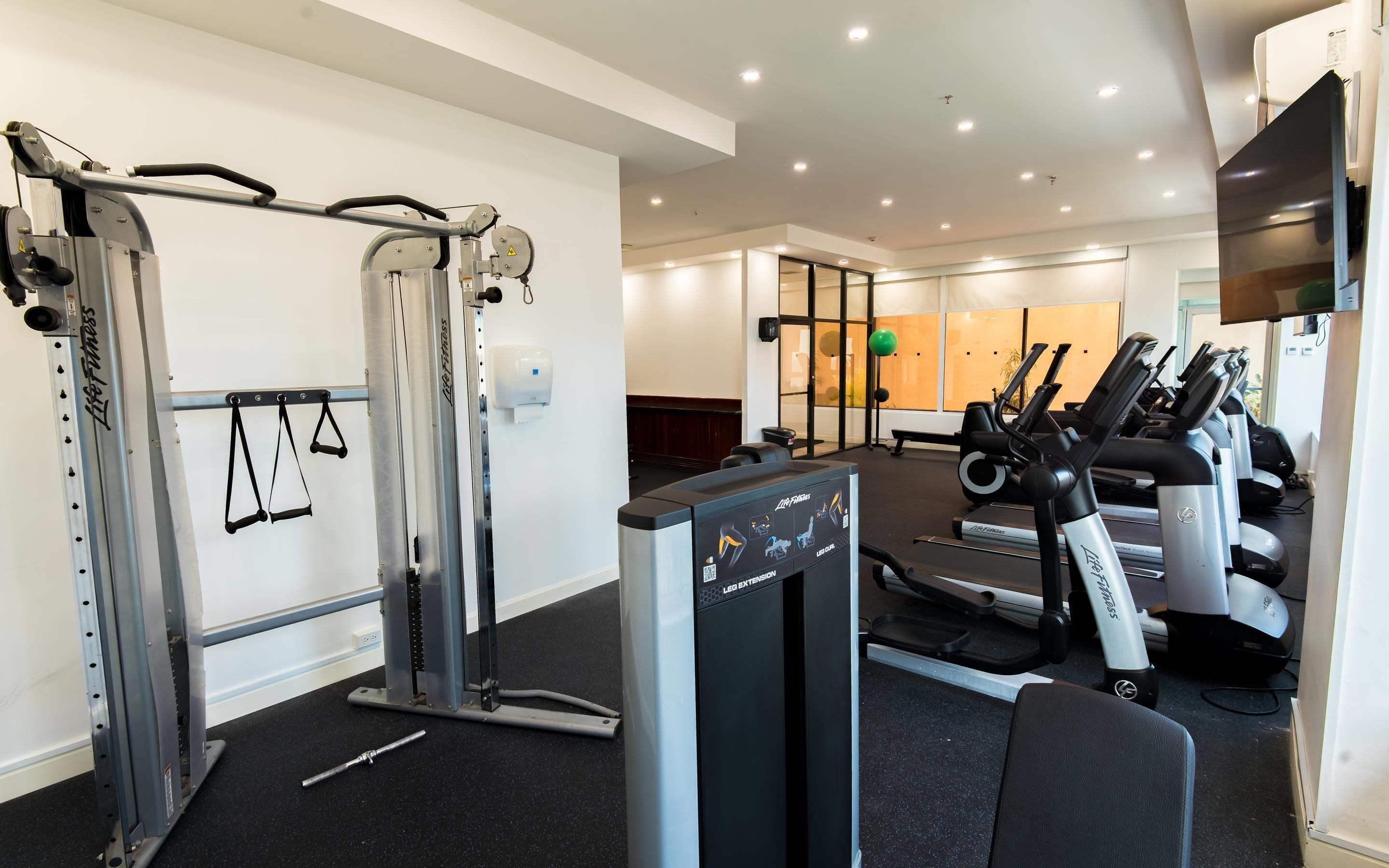 Una sala de gimnàstica amb màquines cardiovasculars, equip d'aixecament de peses i un mirall.