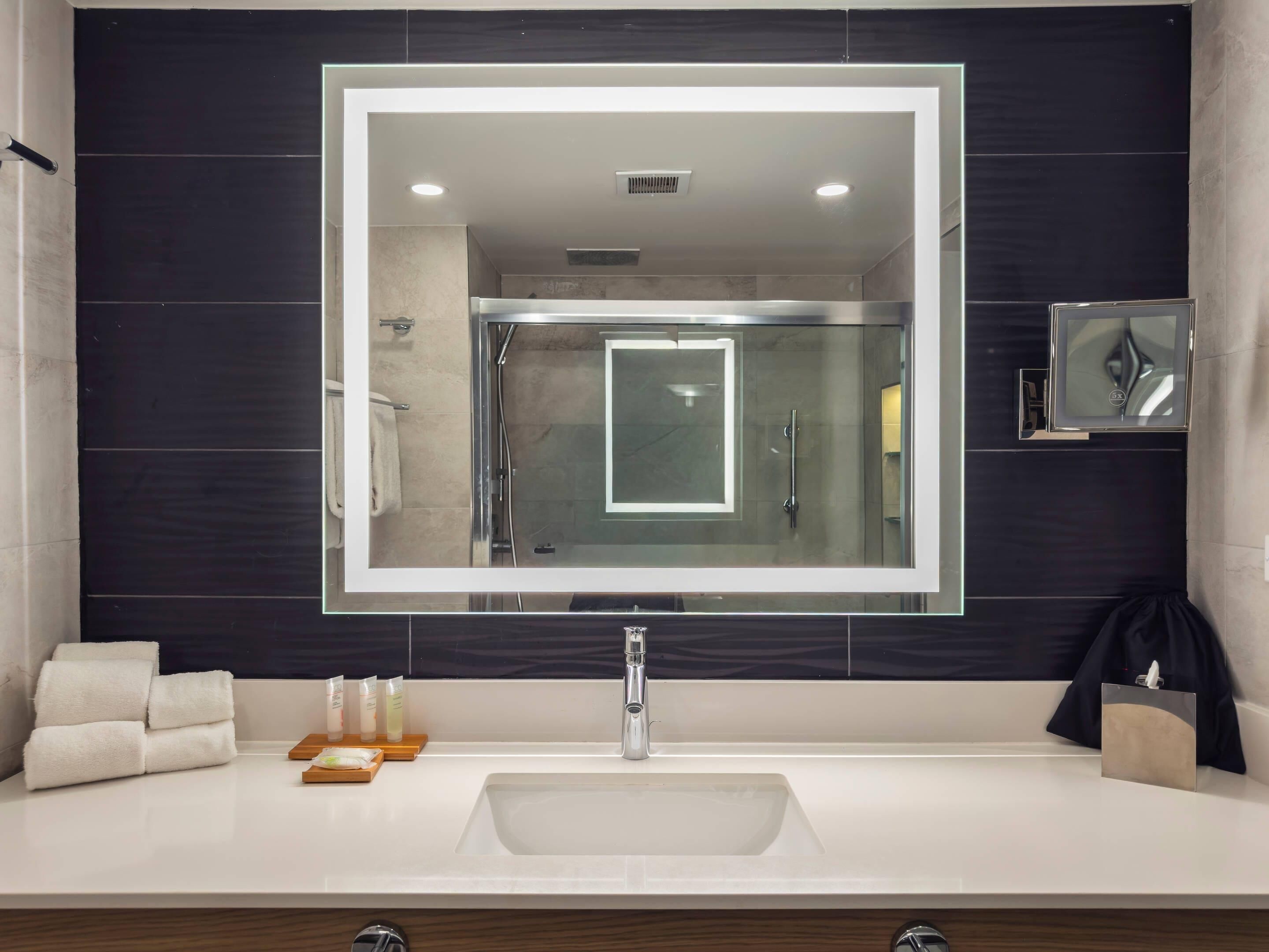 A modern bathroom with a large mirror, a sink, and a shower.