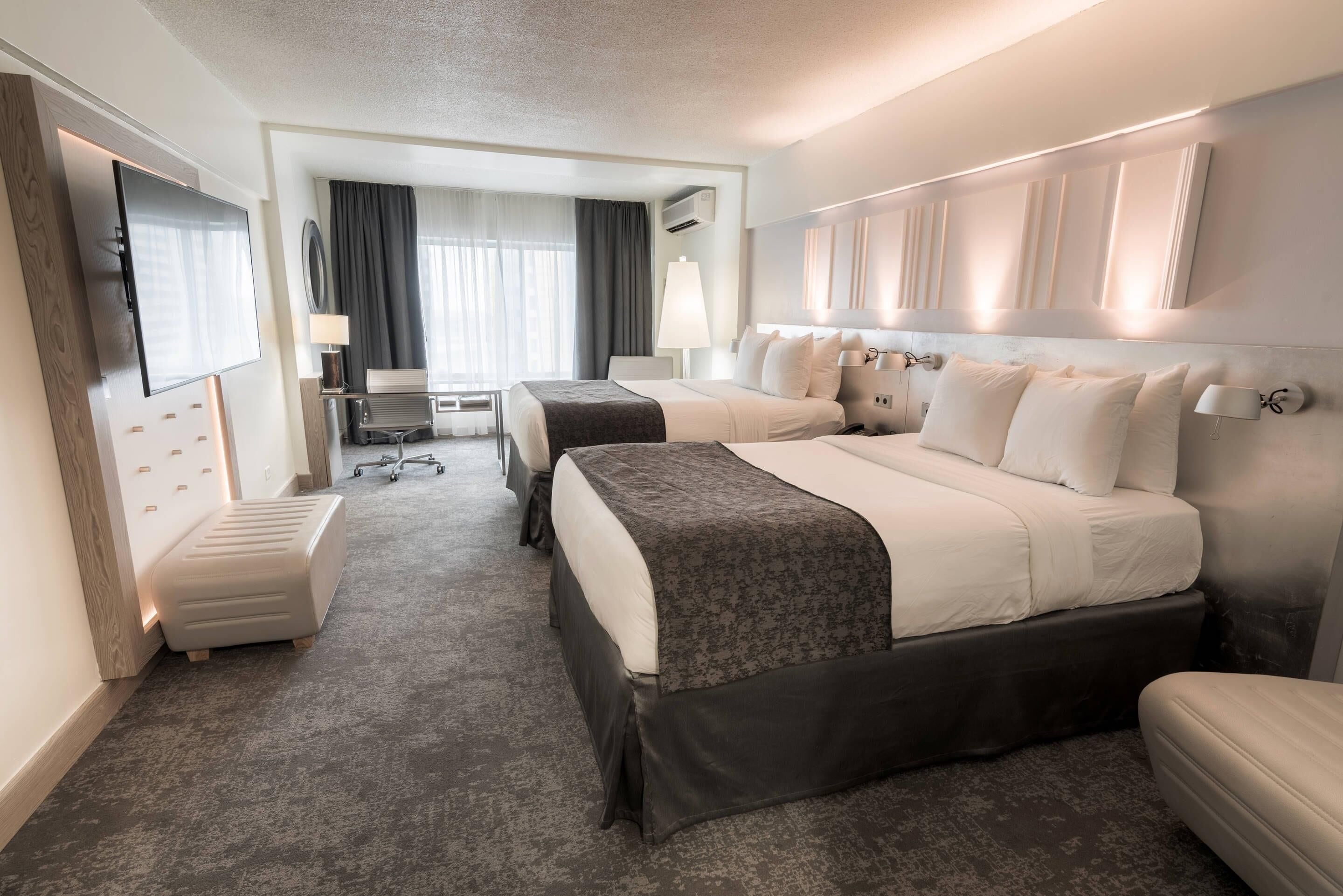 Una habitación de hotel con dos camas, un escritorio, una silla, un televisor y una ventana con cortinas.