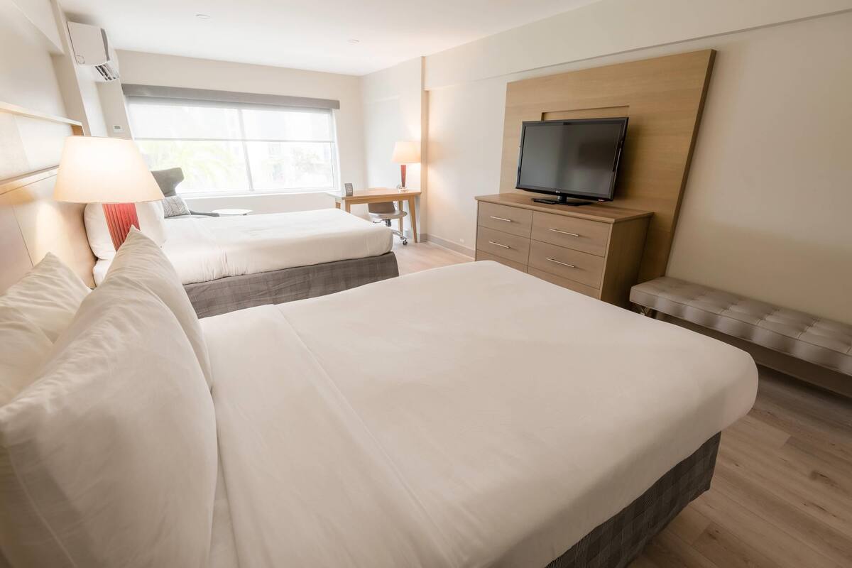A hotel room with two beds, a TV, a desk, and a window.