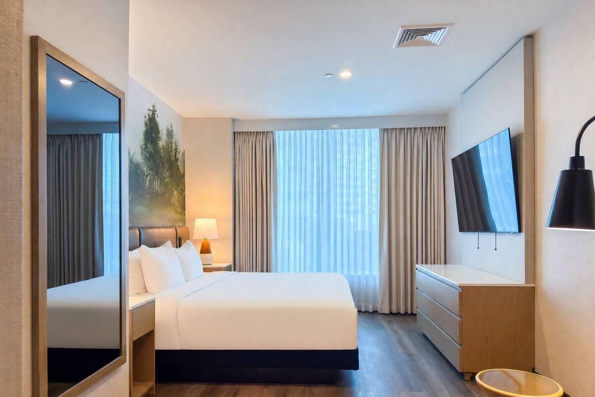 A hotel room with a bed, a TV, a desk, a chair, a mirror, and a window with curtains.