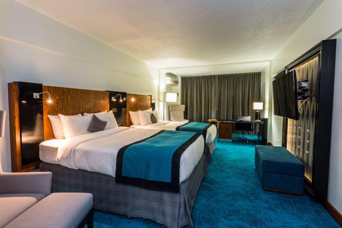 A hotel room with two beds, a desk, a chair, a TV, and a wardrobe.