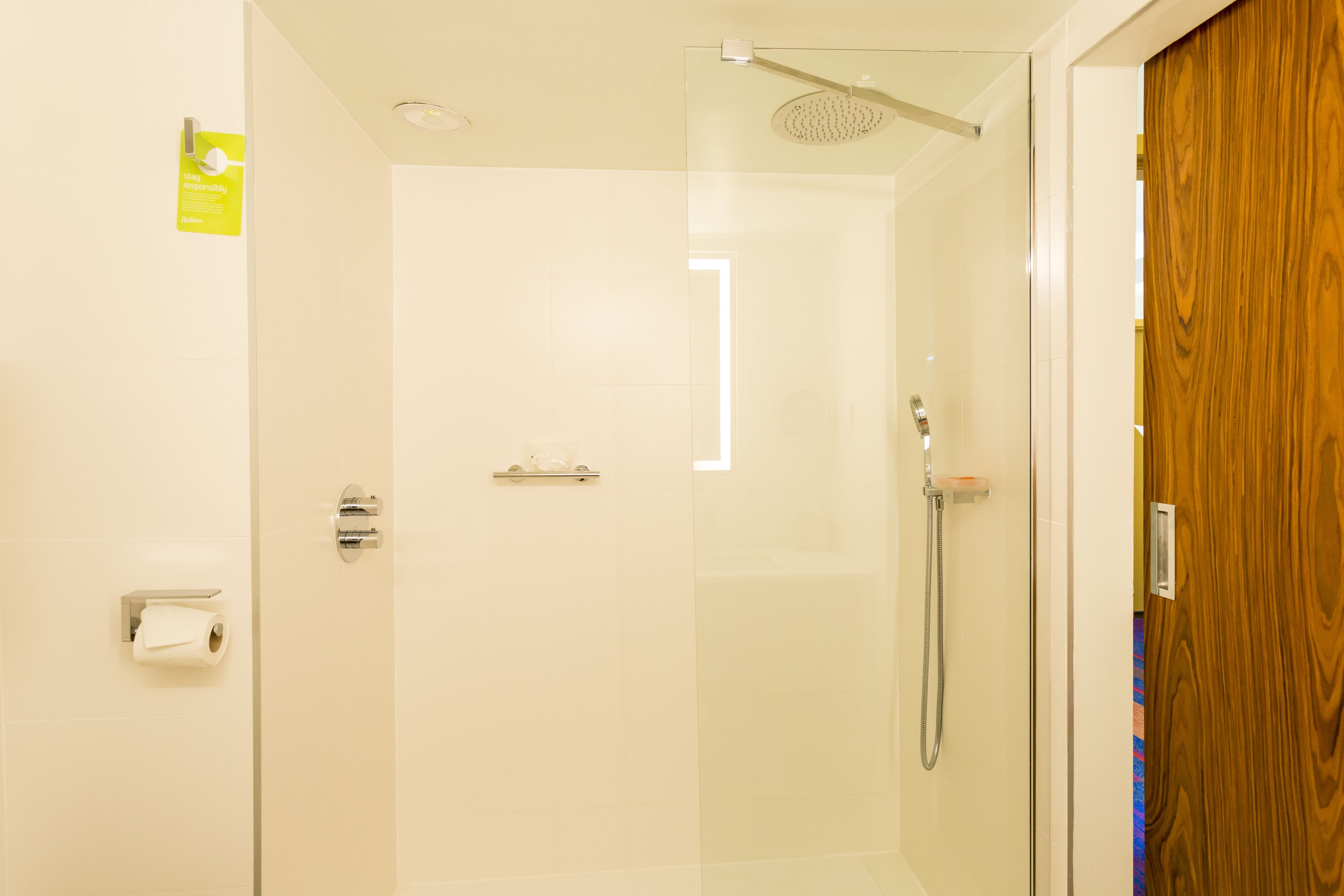 A modern bathroom with a glass shower enclosure, a wooden door, and a visible toilet paper holder.