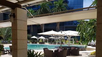 A poolside area with lounge chairs and umbrellas, a pool, and a modern building in the background.