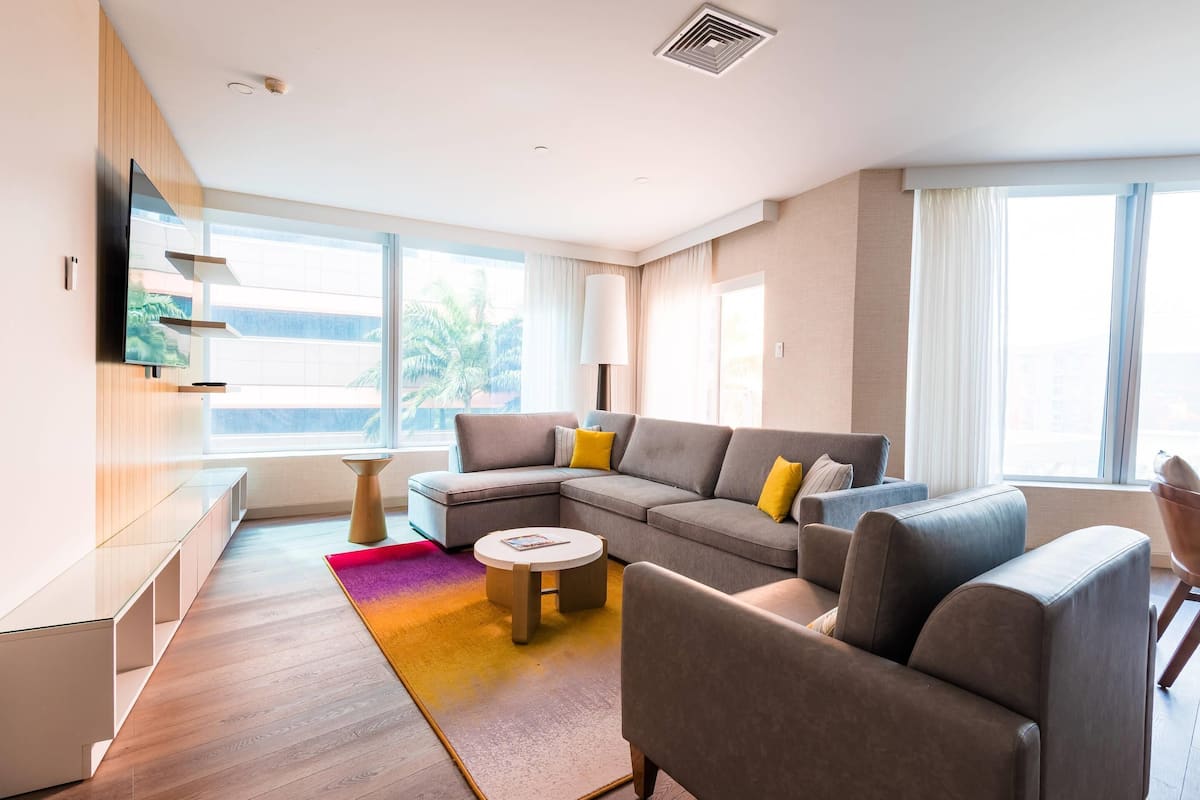 A modern living room with a sectional sofa, a round coffee table, and a flat-screen TV mounted on the wall.