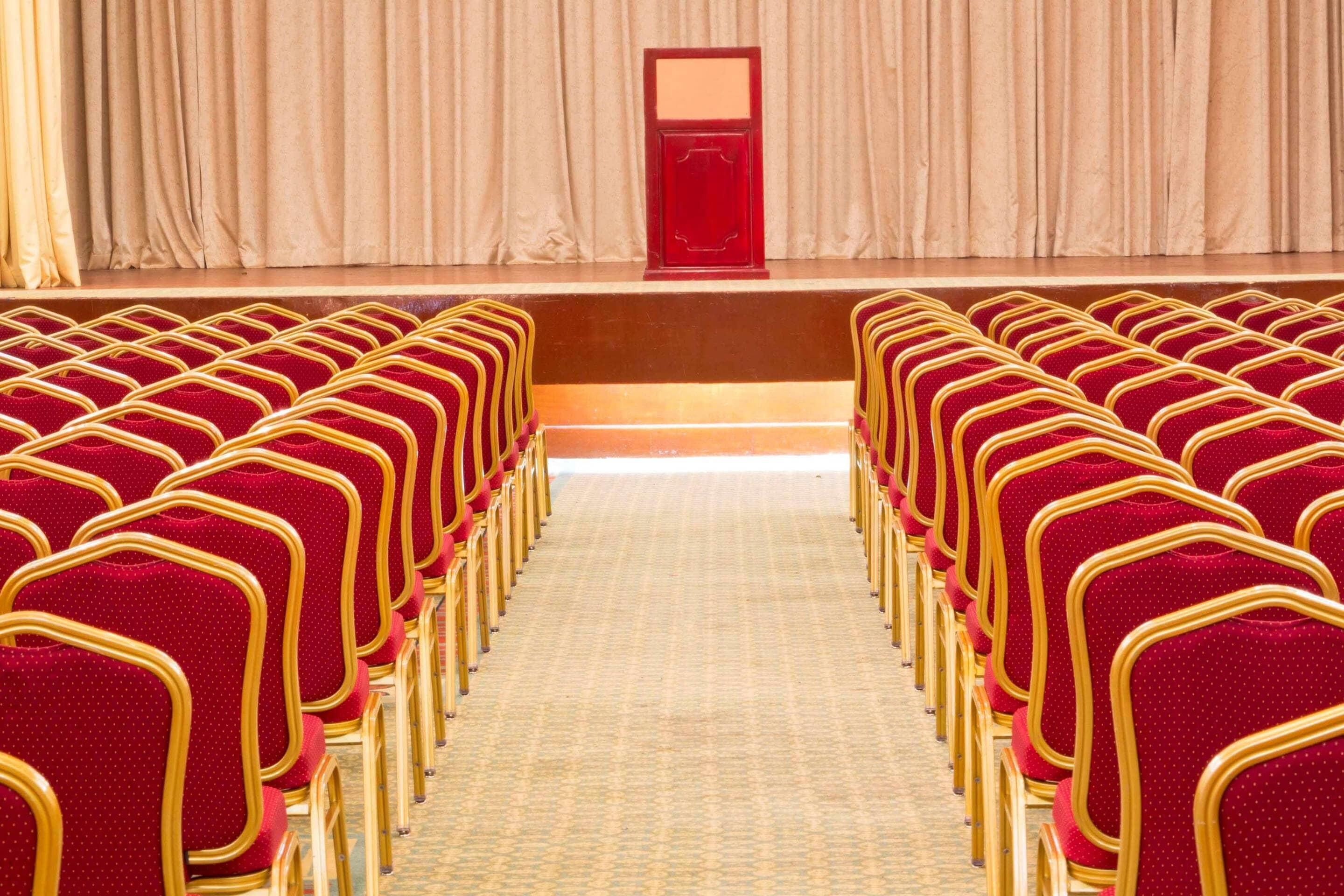 A theater with rows of red chairs and a stage with a red podium.