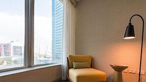 A hotel room with a window, a chair, a lamp, and a small table.