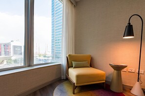 Una habitación de hotel con ventana, una silla, una lámpara y una mesita.