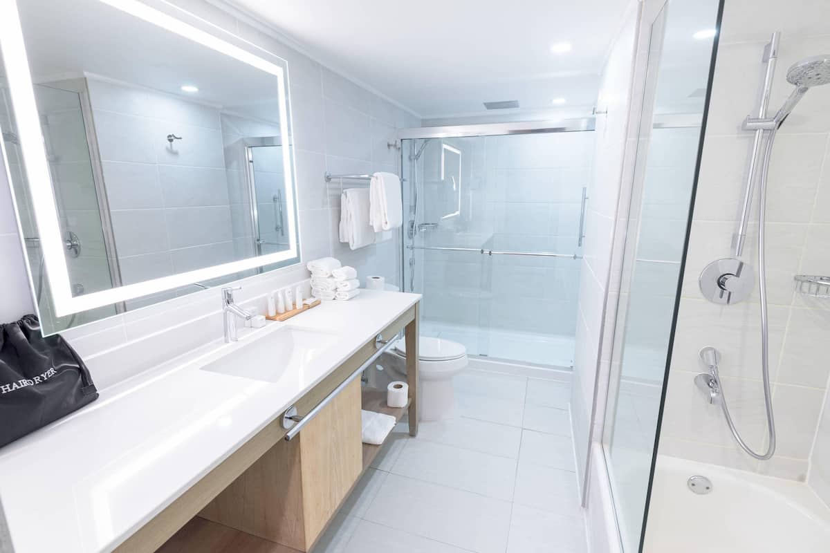 A modern bathroom with a glass shower enclosure, a white sink with a mirror, and a wooden vanity.