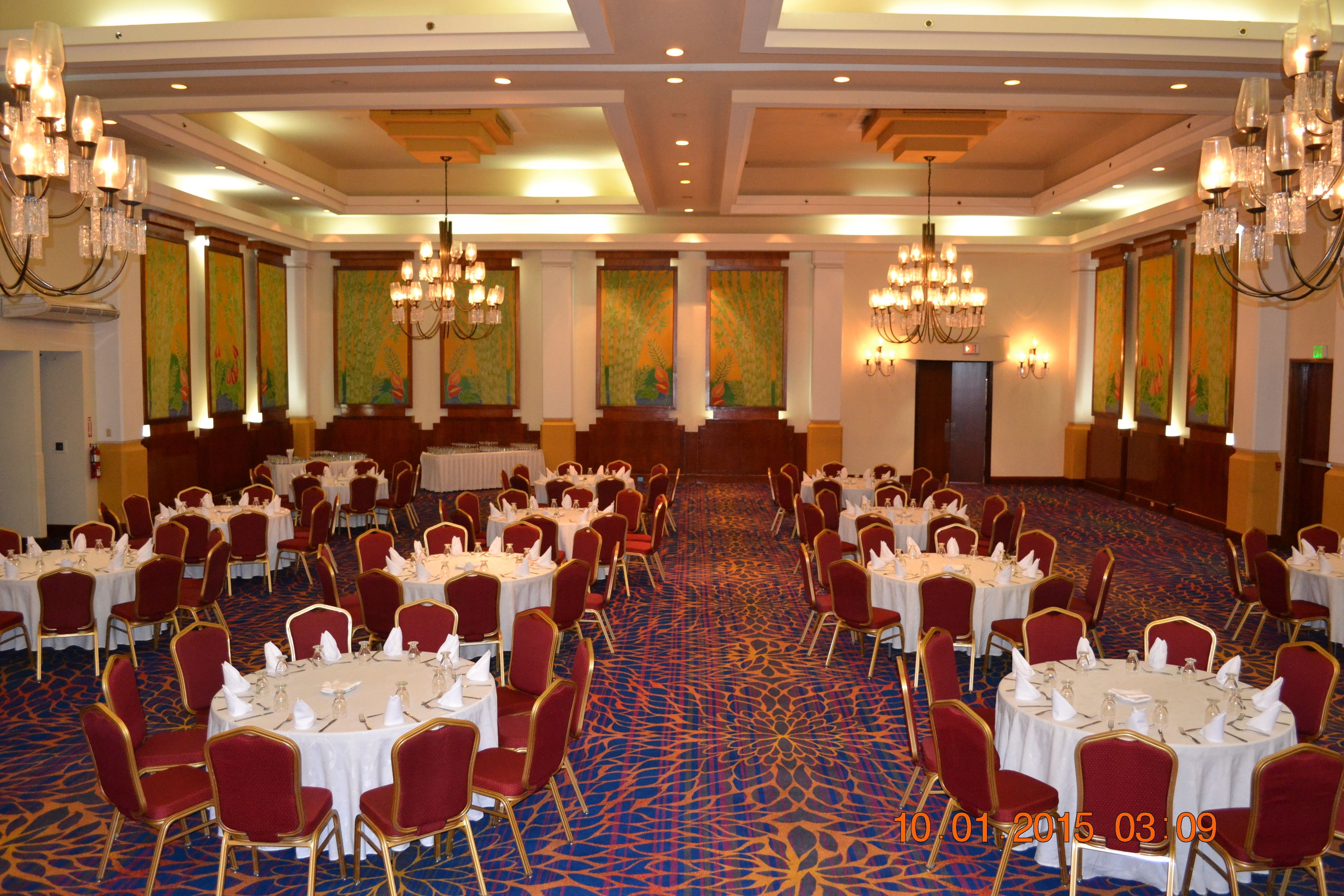 Une salle de banquet avec des tables rondes et des chaises rouges, de grands lustres et des panneaux décoratifs sur les murs.