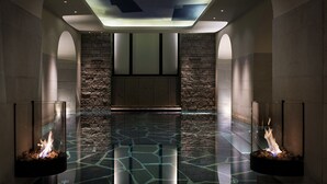 A modern indoor pool area with a geometric glass floor, stone walls, and two glass fire features. - Grand Hôtel Stockholm (Stockholm)