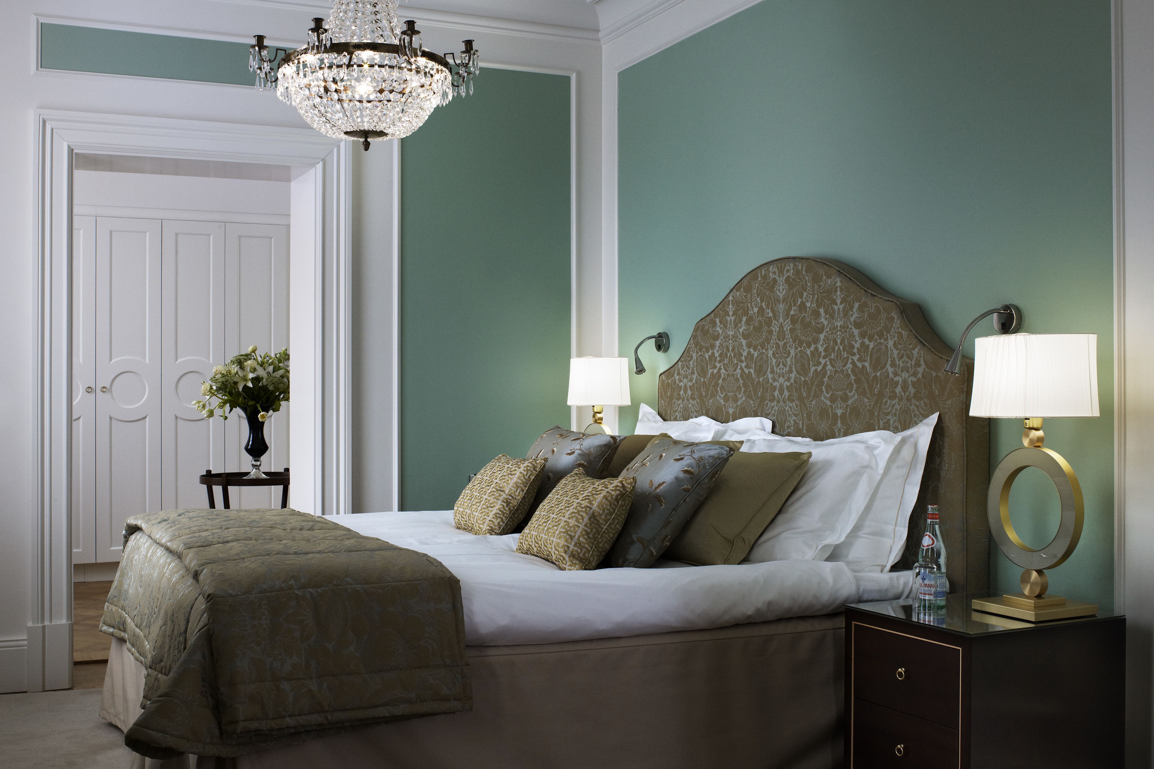 A neatly arranged bedroom with a bed, bedside lamps, a nightstand, and a chandelier.