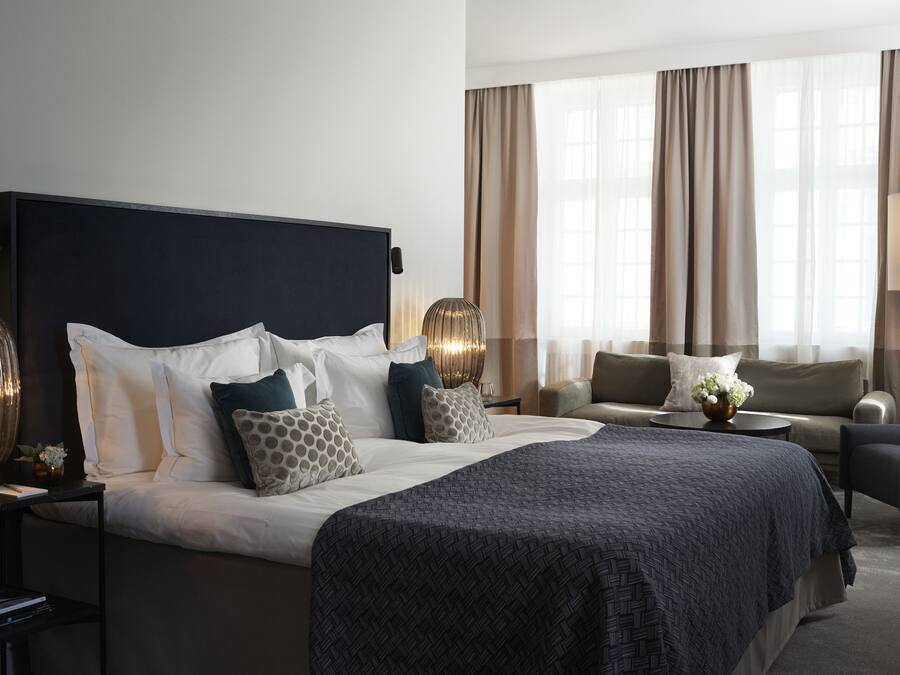 A modern hotel room with a large bed, a sofa, and a desk.