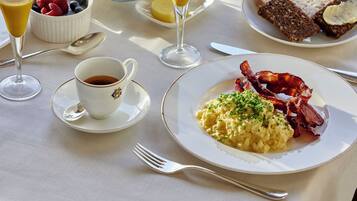 Una mesa de desayuno con diversos platos, incluyendo huevos revueltos, tocino, tostadas y fruta.