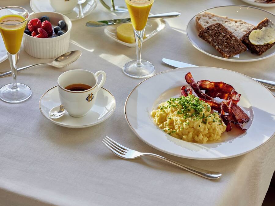 Ett frukostbord med olika rätter, inklusive äggröra, bacon, rostat bröd och frukt.