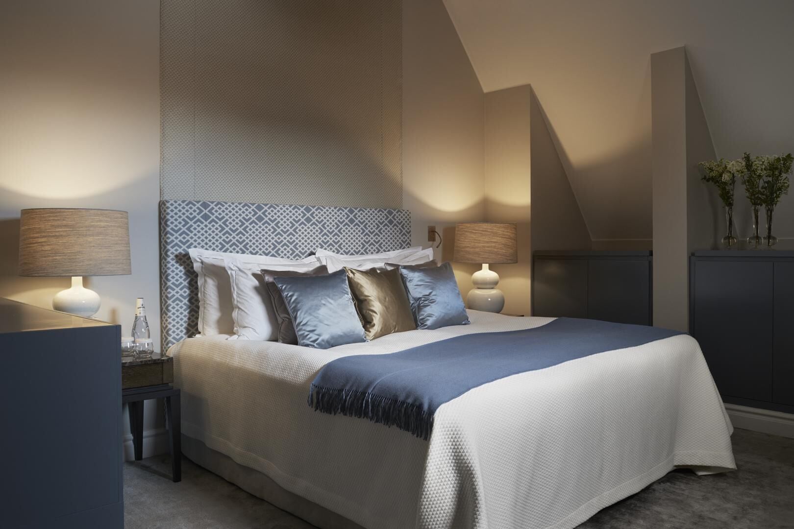 Een moderne slaapkamer met een groot bed, twee nachtkastjes en een hoofdbord met een geometrisch patroon.