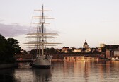 A tall ship docked in a harbor with a cityscape in the background.