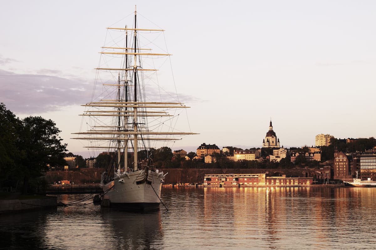 A tall ship docked in a harbor with a cityscape in the background.