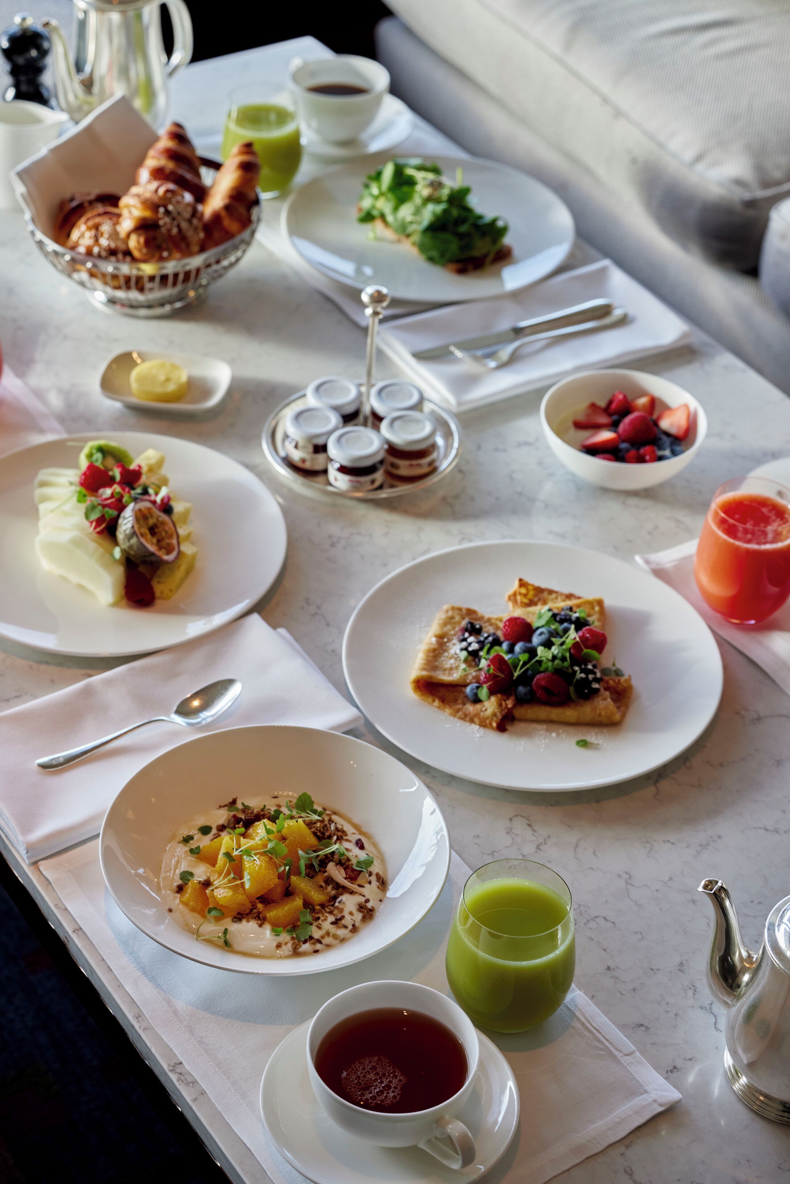 A breakfast table with various dishes, including croissants, fruit, and a green smoothie.