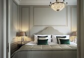 A neatly made bed with a white headboard, two bedside tables with lamps, and a chandelier above.