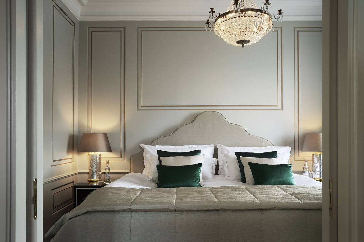 A neatly made bed with a white headboard, two bedside tables with lamps, and a chandelier above.