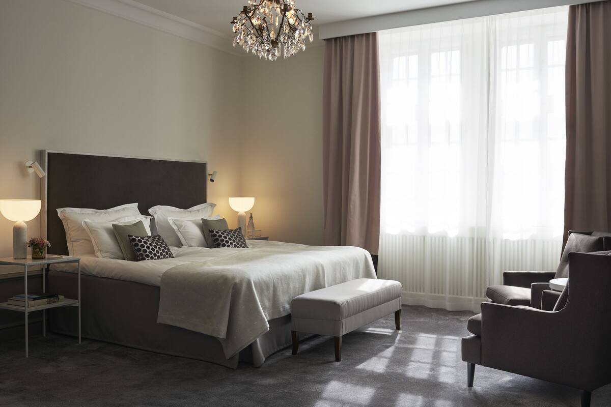 A neatly arranged bedroom with a large bed, bedside lamps, a bench, and a chair.