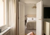 A bedroom with a bed, a nightstand, a dresser, a chandelier, and a window with curtains.